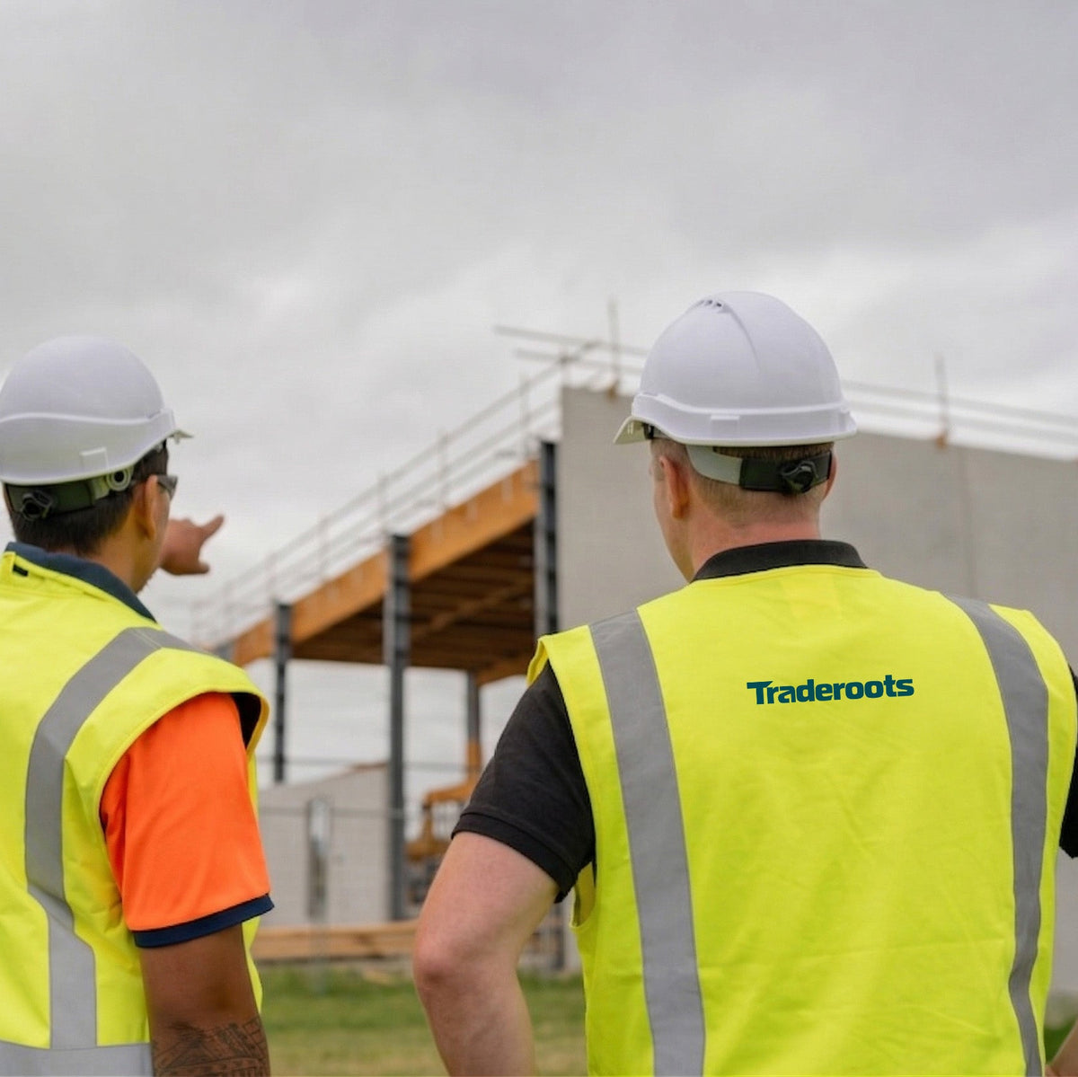 Two construction workers in high-visibility vests and hard hats looking at a building under construction.